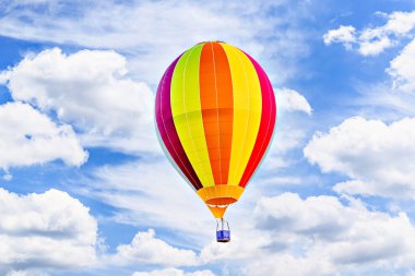 Mavi gökyüzünde beyaz bulutlarla uçan renkli sıcak hava balonu