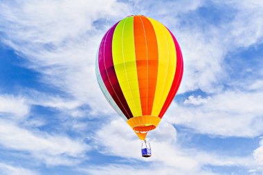 Mavi gökyüzünde beyaz bulutlarla uçan renkli sıcak hava balonu