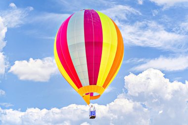 Mavi gökyüzünde beyaz bulutlarla uçan renkli sıcak hava balonu