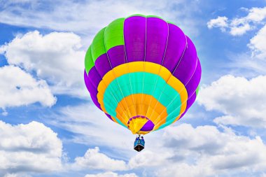 Mavi gökyüzünde beyaz bulutlarla uçan renkli sıcak hava balonu