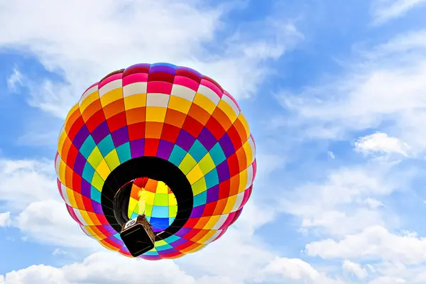 Mavi gökyüzünde beyaz bulutlarla uçan renkli sıcak hava balonu