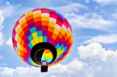 Mavi gökyüzünde beyaz bulutlarla uçan renkli sıcak hava balonu