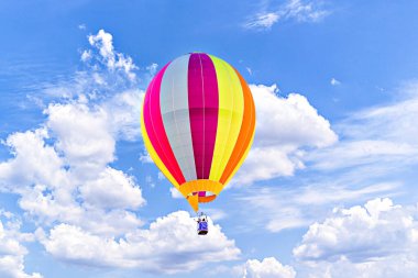 Mavi gökyüzünde beyaz bulutlarla uçan renkli sıcak hava balonu