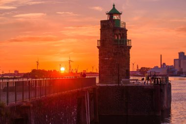 Yazın günbatımında dramatik bir gökyüzünün altındaki nehir limanındaki taş deniz feneri. Bremen, Almanya