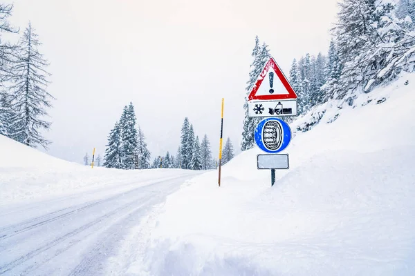Warning sign and tyre chains sign along a snowy mountain road during a snowstorm