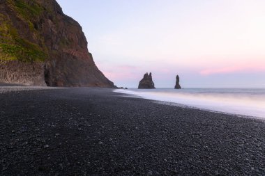 Sea stacks along a black pebble beach in Iceland under midnight sun in summer. Reynisfjara beach, Vik, Iceland.