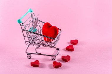Red heart on a shopping trolley against pink background. Valentines day shopping concept. Copy space.
