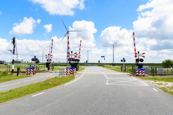 Level Crossing with Signals and Warning Signs along both a road and a bicycle lane in the countryside of Netherlands. A wind farm is in background. Eemshaven, Netherlands.