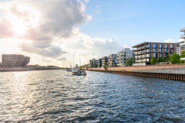 New apartment buildings in a redevelopped area along a former river harbour at sunset. Boats moored to a jetty are visible in the middle of the harbour. Bremen, Germany.