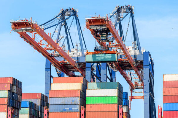 Huge port cranes loading a cargo ship up with containers on a sunny summer day. Rotterdam, Netherlands.