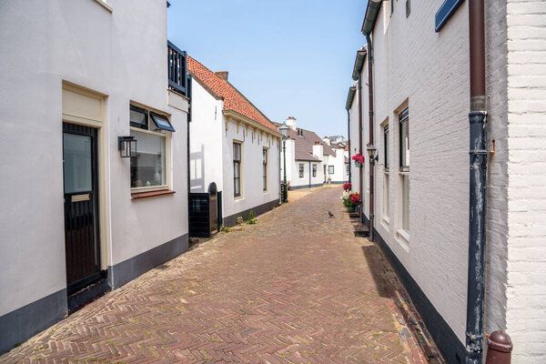 Narrow brick street lined with white holiday cottages in a seaside town on a sunny summer day. Katwijk aan Zee, Netherlands.