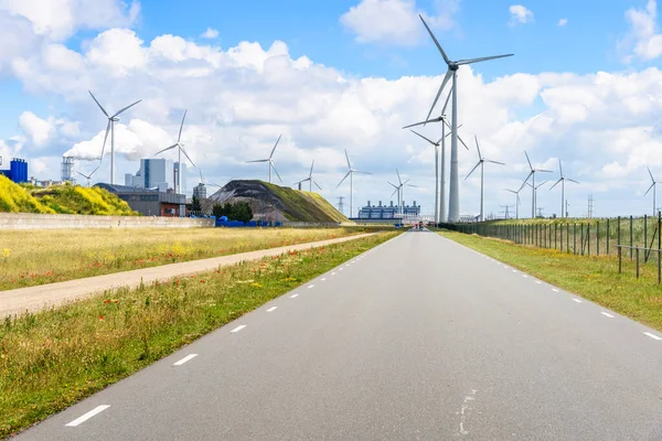 Road lined with wind turbines in an industrial district on a sunny summer day. A coal fired power plant is visible in distance. Eemshaven, Netherlands.