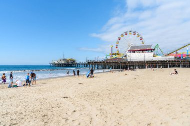 Santa Monica, CA - 16 Ekim 2022: İnsanlar iskelenin yanındaki kumsalda sıcak bir sonbahar gününün tadını çıkarıyorlar. Santa Monica Eyalet Plajı dünyanın en ikonik ve pitoresk yerlerinden biridir ve küresel ziyaretçileri her gün çeker..
