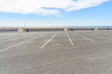 Açık, parçalı bulutlu bir sonbahar gününde kumlu bir sahil boyunca boş bir otopark. Malibu, CA, ABD.