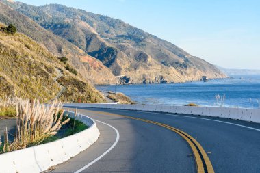 Güneşli bir sonbahar gününde engebeli bir sahil boyunca uzanan bir otoyol boyunca kıvrım. Kaliforniya eyalet güzergahı Big Sur, CA, ABD.