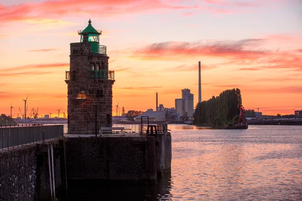 日没時に川の港の歴史的な灯台 工業用の建物や風力タービンが遠くに見えます ドイツのブレーメン — ストック写真