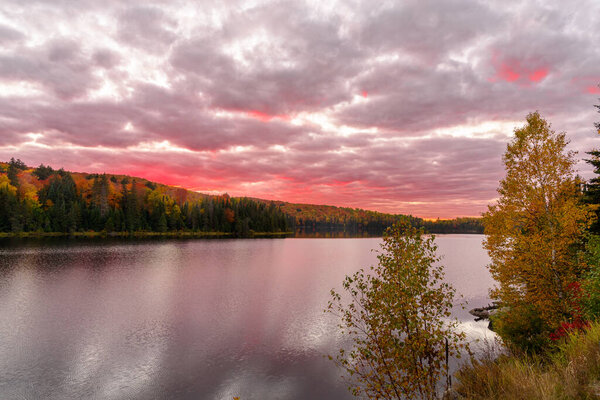 Драматическое красочное небо над озером, окруженное лесистыми холмами на пике осенних красок на закате