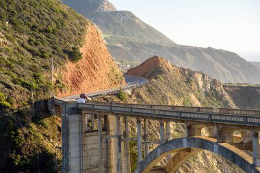 Sonbaharda günbatımında dolambaçlı sahil yolu boyunca beton kemer köprüsü. Bixby Köprüsü, Big Sur CA, ABD..