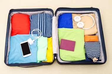 Giysiler, aksesuarlar ve pasaportlarla dolu açık bir bavulun üstündeki görüntüyü göster. Seyahat konsepti.