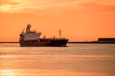 Limana giden bir petrol tankerinin üzerinde turuncu yaz günbatımı gökyüzü. Rotterdam, Hollanda.