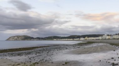 Yazın gün batımında kumlu bir sahil ve sahil kasabasında hareket eden bulutlar. Llandudno, Galler, İngiltere - zaman aşımı