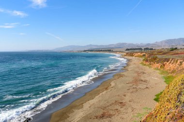 Kaliforniya sahilindeki dik yamaçların eteklerindeki ıssız sahil açık bir sonbahar gününde. California eyalet güzergahı uçurumlar boyunca uzanıyor..