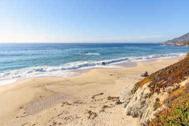Büyük okyanus dalgaları, güneşli bir sonbahar gününde, kayalıklarda, ıssız bir kumsalda kırılıyor. Kaliforniya, ABD.