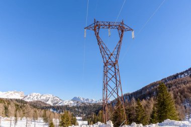 Açık bir kış gününde, karlı bir dağ manzarasında uzun elektrik direği