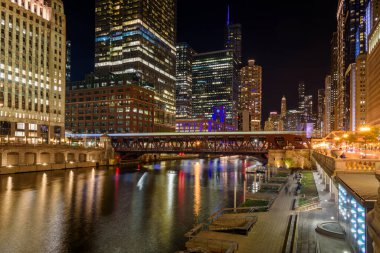 Chicago şehir merkezi ve nehir manzaralı. Köprüden geçen bir trenin bıraktığı hafif izler ön planda görünür..