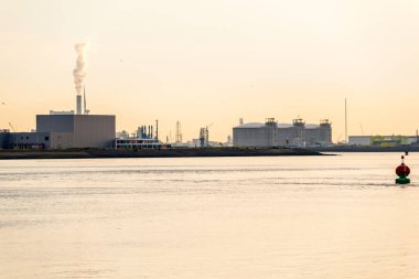 Günbatımında büyük bir limanın rıhtımlarında sanayi tesisleri ve yakıt depoları. Rotterdam, Hollanda.