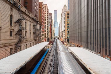 Bulutlu bir bahar gününde Chicago şehir merkezindeki yüksek bir istasyondan kalkan gümüş ışık treni. Illinois, ABD.
