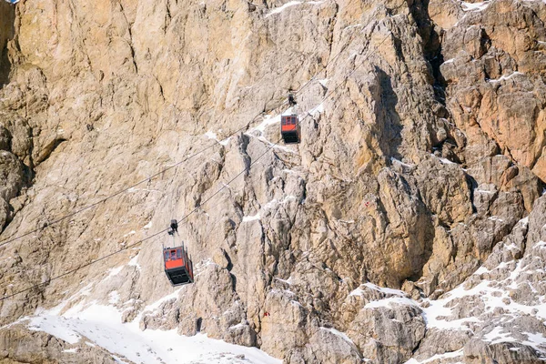 Aerial tramway passenger cabins transporting tourists up and down a snowy rocky peak in the Alps on a sunny winter day. Dolomites, Italy.