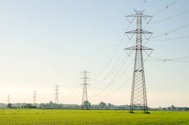 Yüksek voltaj hatları, ilkbaharda günbatımında kırsal alanda yüksek çelik kuleler tarafından desteklenir.