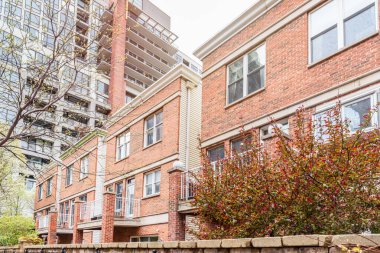 Bulutlu bir bahar gününde duvarlı bir sitede Brick Rrow evleri. Arka planda modern bir apartman binası var. Chicago, IL, ABD.
