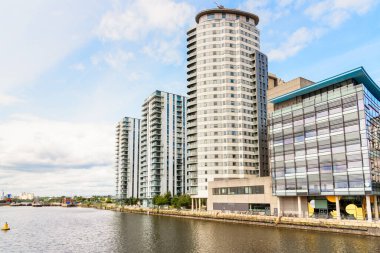 Parçalı bulutlu bir yaz gününde rıhtımdaki cam ofis binasının yanındaki modern konut binaları. Manchester, İngiltere, İngiltere.