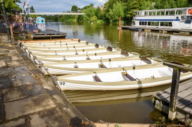 Yazın bulutlu gökyüzünün altındaki nehir boyunca taş rıhtımına bağlı boş gezgin tekneler. Chester, İngiltere, İngiltere.