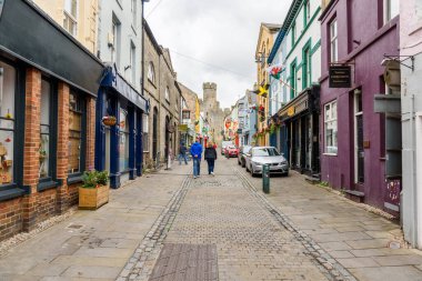 Caernarfon, Wales, UK - July 10, 2023: people walking along a narrow cobbled street in the walled old town. Caernarfon is a royal town, cwhich lies on the eastern shore of the Menai Strait, opposite the island of Anglesey clipart