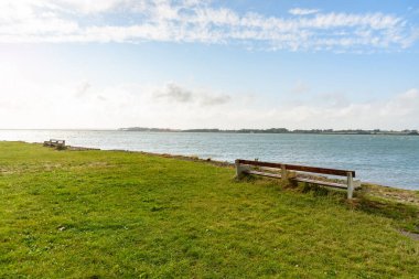 Açık bir yaz gününde küçük bir sahil parkında denize bakan boş bir ahşap. Caernarfon, Galler, İngiltere.