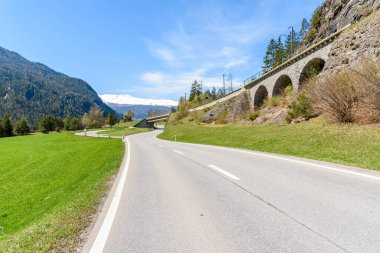 Güneşli bir bahar gününde İsviçre Alplerinde bir demiryolunun altından geçen boş bir viraj yolu. Fillisur, İsviçre