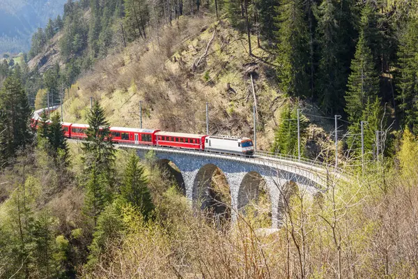 Elektrikli yolcu treni güneşli bir günde dağlarda eğimli bir taş viyadük üzerinde koşuyor. Fillisur, İsviçre
