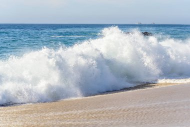 Büyük bir okyanus dalgası Kaliforniya 'da kumlu bir kıyıya vuruyor güneşli bir sonbahar gününde