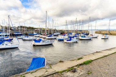 Yelkenli, sonbaharda bulutlu gökyüzünün altında eski bir limana demir attı. Musselburgh, İskoçya, İngiltere.