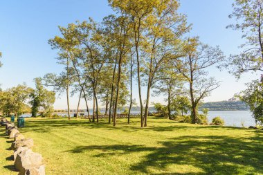 Güneşli bir sonbahar sabahında nehir kenarındaki parkta piknik masaları ve barbekü ızgaraları olan otlama alanı. Palisades Parkı, NJ, ABD.