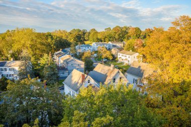 View form above of a residential district with semi-detached houses along a street surrounded by decidous trees at sunset in autumn. Poughkeepsie, NY, United States. clipart