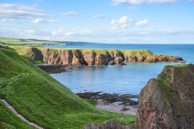 Güneşli bir yaz gününde İskoçya kıyısı boyunca bir körfez. Çimenli bir uçurumdan kayalık bir plaja uzanan boş bir merdiven ön plandadır. Stonehaven, İskoçya, İngiltere.