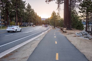 Sonbaharda gün batımında bir caddeye paralel giden terk edilmiş bir sahil bisiklet yolu. South Lake Tahoe, Ca, ABD.