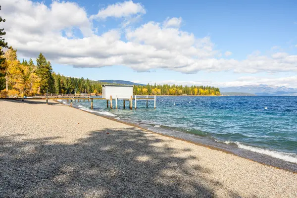 Güneşli bir sonbahar gününde, dağ gölü üzerinde ahşap rıhtımları ve kayıkhaneleri olan boş çakıl taşı plajı. Tahoe Gölü, CA, ABD.