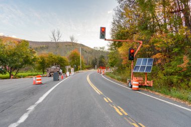 Sonbaharda günbatımında dolambaçlı bir dağ yolundaki yol çalışması alanının başında güneş panellerinden gelen trafik sinyalleri kırmızıya vuruyor. Catskill Dağları, New York, ABD.