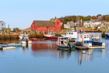 Fishing boats in harbour at twilight in autumn. A red wooden fishing shack on a stone quay is in background. Rockport, MA, USA. clipart