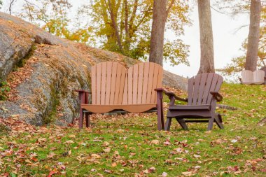 Empty armchairs on grass covered in fallen leaves in a park in autumn. Bolton Landing, NY, USA. clipart